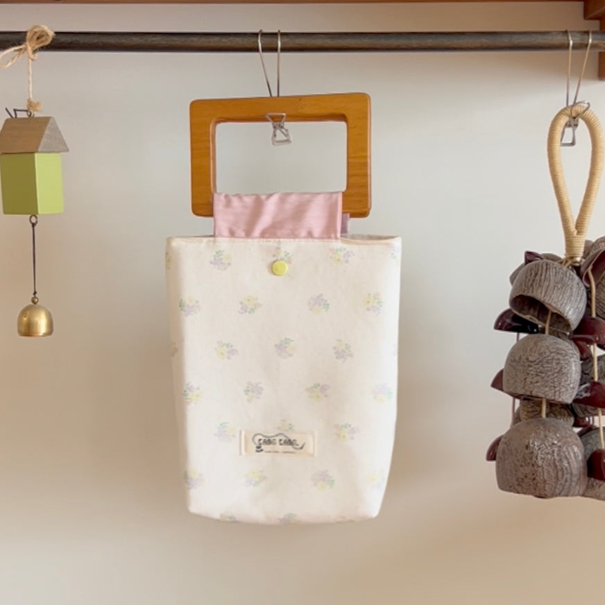 Blossom Wood Bag in Sakura Mist – white fabric tote with soft floral print and wooden square handle, styled in a warm handcrafted home setting