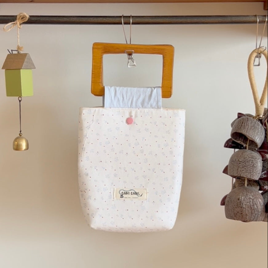 Blossom Wood Bag in Sky Blossom – white fabric tote with delicate dot print and wooden square handle, hanging in a cozy lifestyle setting with wind chimes