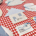 Blue Gingham House Coaster placed on a red gingham tablecloth