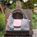 Kang Kang handmade Polka Dot Handbag in grey fabric with black dots and pink front pocket, displayed open on a wooden board in a garden with white cosmos flowers