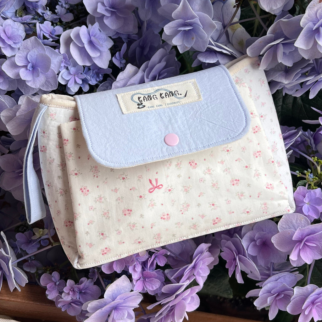 Kang Kang handmade Flap Pouch Bag in ditsy floral cream fabric with light blue flap and pink snap button, surrounded by purple hydrangeas