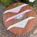 Kang Kang handmade dog triangle scarf set of 3, flat lay on wooden surface showing all three colorways