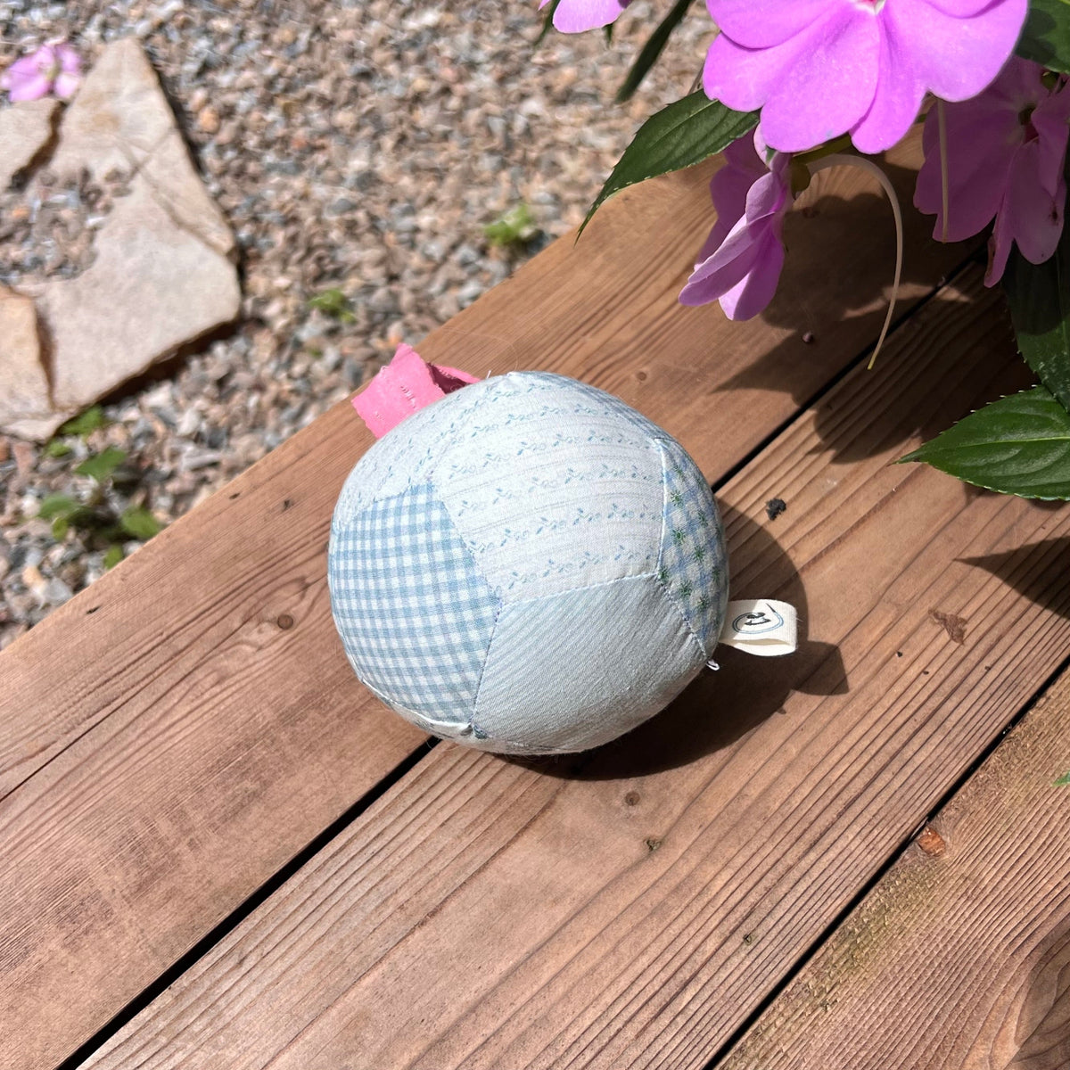 Kang Kang Handmade Patchwork Dog Ball on wooden deck showing elastic cord and label, outdoor setting