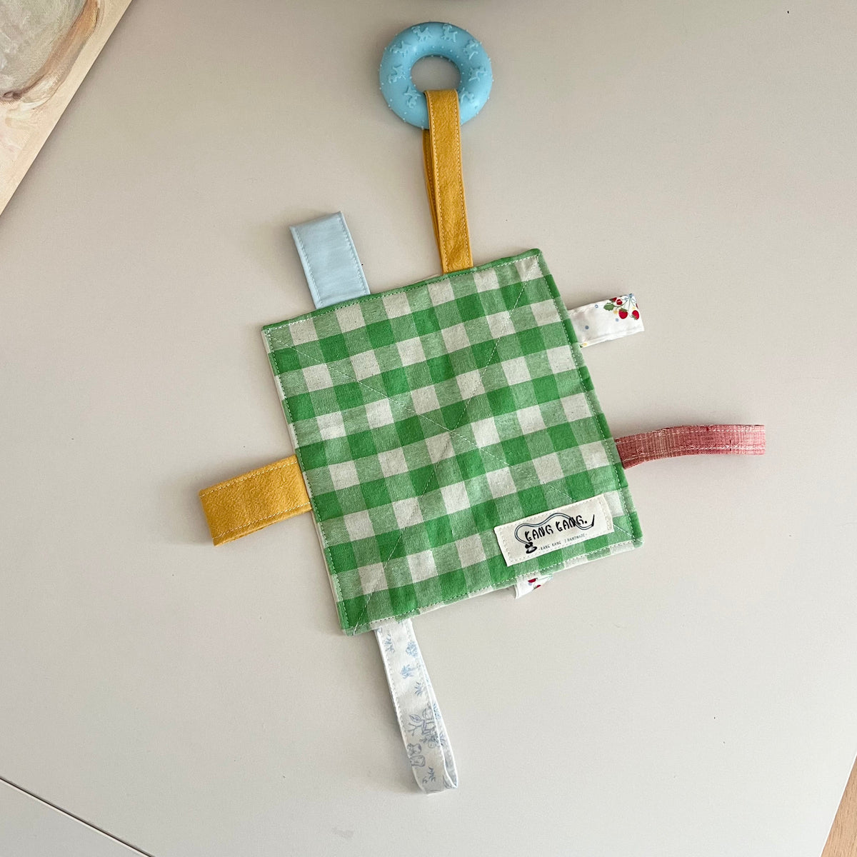 Kang Kang Handmade Crinkle Play Mat laid flat showing green gingham quilted fabric and colorful ribbon tabs