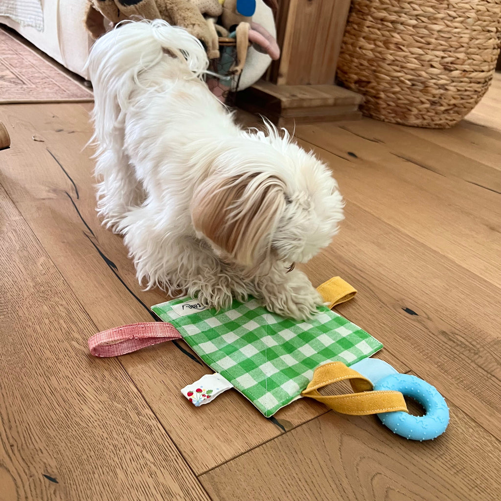 Small white dog playing with the Kang Kang Handmade Crinkle Play Mat on a wooden floor