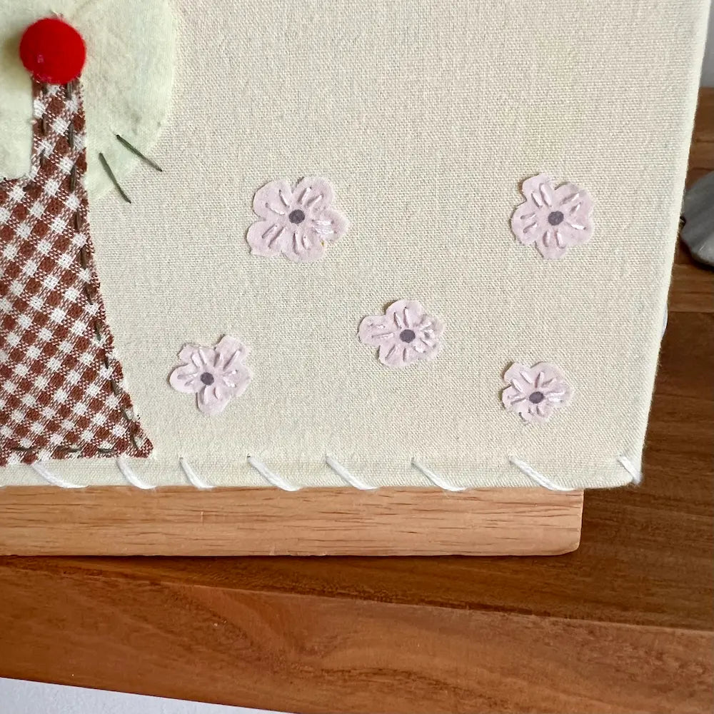 Close-up of handmade fabric lamp base showing delicate hand-sewn flower appliqués on natural linen fabric with wooden base detail